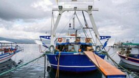 Moored blue and white boat with lowered bridge, made of metal near the shore of the Aegean sea, Stavros, Greece